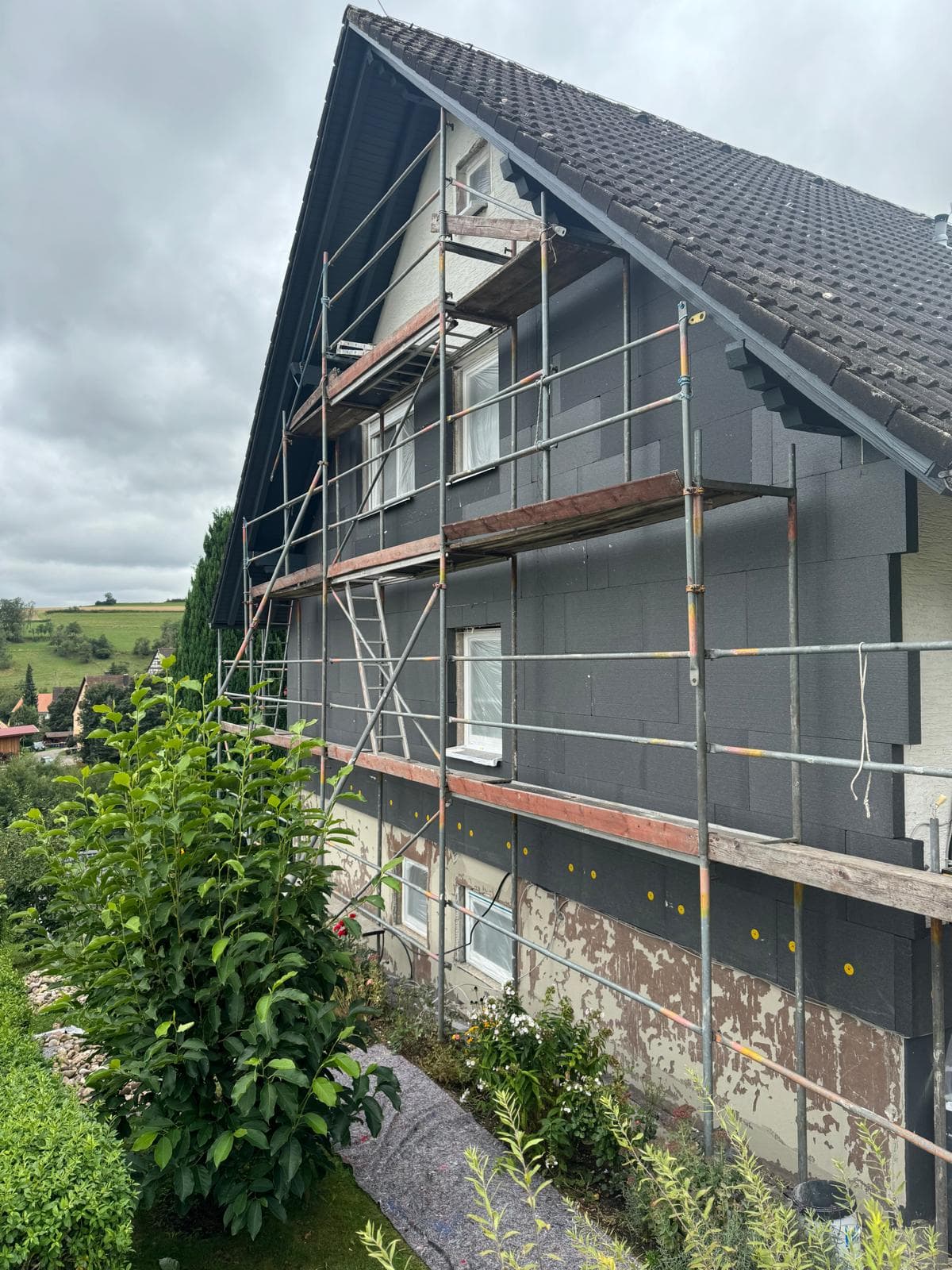 Eingerüstetes Haus mit fertig montierter, anthrazitfarbener Fassadendämmung
